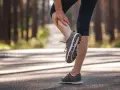 Biegacz masuje swoje twarde, napięte łydki po treningu w lesie.
