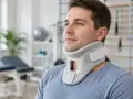 Mężczyzna w kołnierzu ortopedycznym, wspierającym jego kręgosłup szyjny. W tle gabinet rehabilitacyjny.