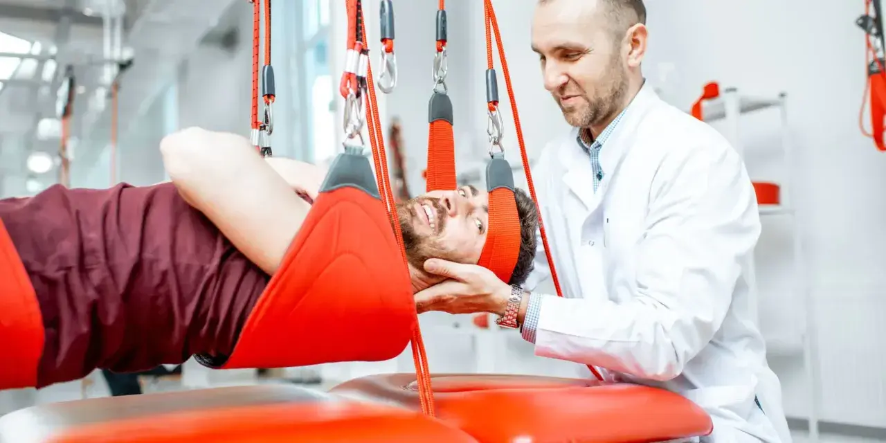 Fizjoterapeuta pomaga pacjentowi podczas terapii wiszącej. Często rehabilitacja kręgosłupa jest kluczowa dla powrotu do zdrowia.