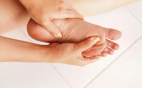 Dłoń masuje bolesną stopę, łagodząc objawy entezopatii rozcięgna podeszwowego.