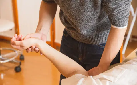 Fizjoterapeuta delikatnie masuje nadgarstek pacjenta, co jest kluczowe, kiedy zacząć rehabilitacja po operacji cieśni nadgarstka.
