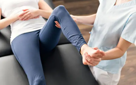 Fizjoterapeuta delikatnie masuje stopę pacjentki, która leży na kozetce. Czy rehabilitacja pomaga? Tak, to klucz do powrotu do zdrowia.