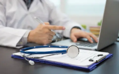 Lekarz pisze skierowanie na rehabilitację, podkreślając, ile jest ważne skierowanie na rehabilitację. Obok leży stetoskop.