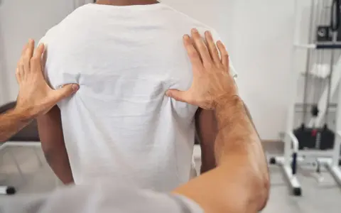 Fizjoterapeuta bada plecy pacjenta, szukając przyczyn bólu w klatce piersiowej od kręgosłupa. Objawy mogą być różne.