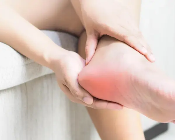 Dłoń masuje bolesną piętę, gdzie może występować neuropatia Baxtera.