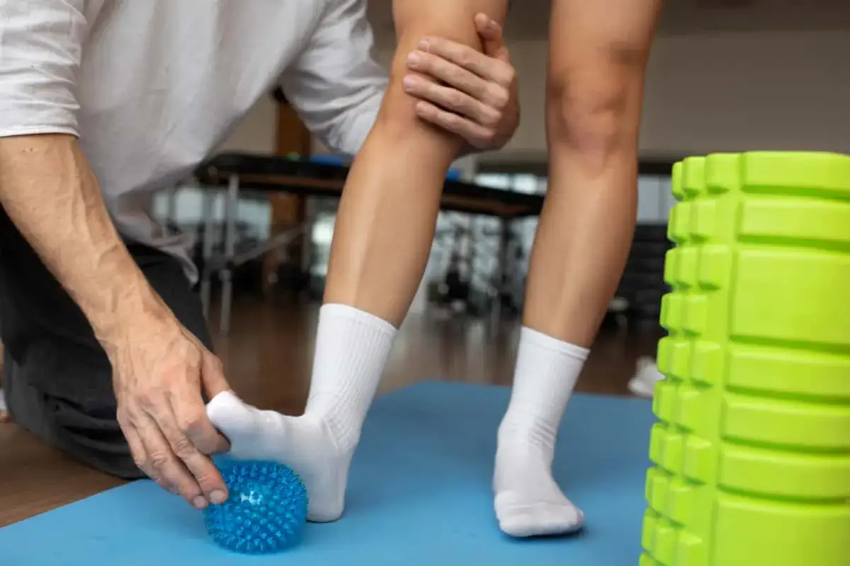 Fizjoterapeuta masuje stopę pacjenta z opuchlizną 2 miesiące po skręceniu kostki, używając niebieskiej piłeczki.