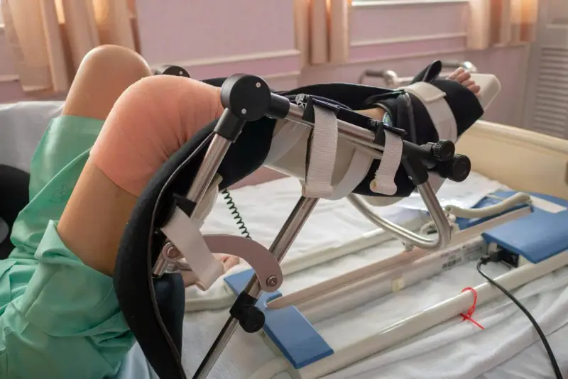 Osoba w łóżku z unieruchomioną nogą w aparacie ortopedycznym. Pamiętaj, czego nie wolno robić po endoprotezie kolana, by uniknąć powikłań.