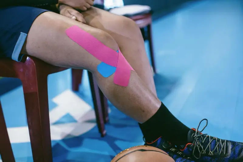 Sportowiec z plastrami na kolanie, przygotowujący się do ćwiczeń na chondromalację rzepki.